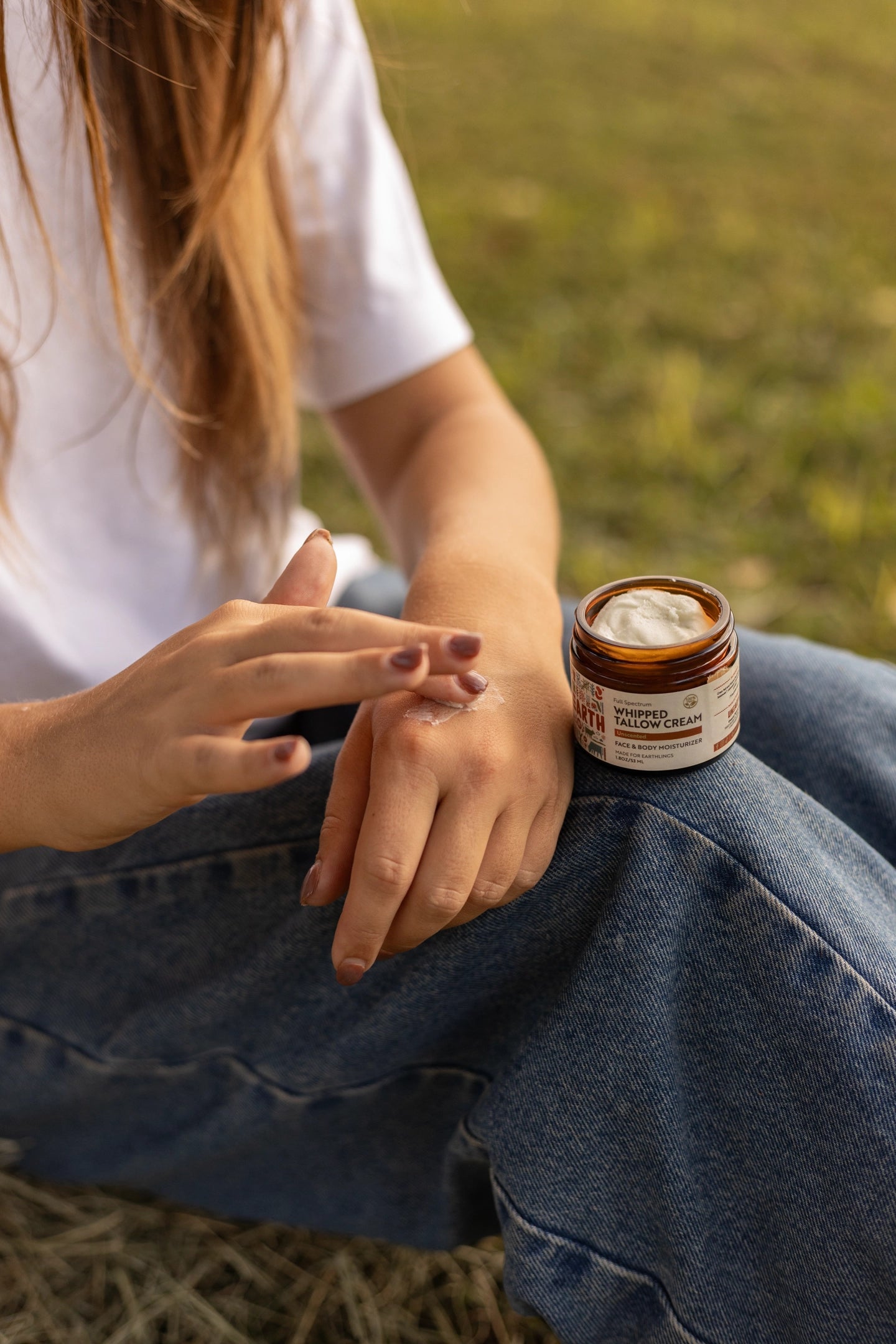Person applying cream to skin with an open jar nearby