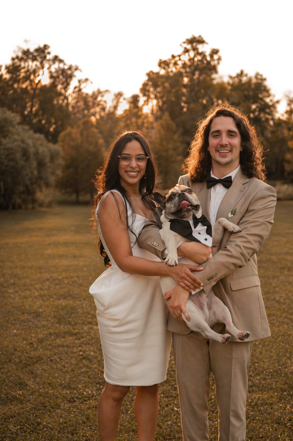 Daniel and Adelida holding a dog in a field with trees in the background